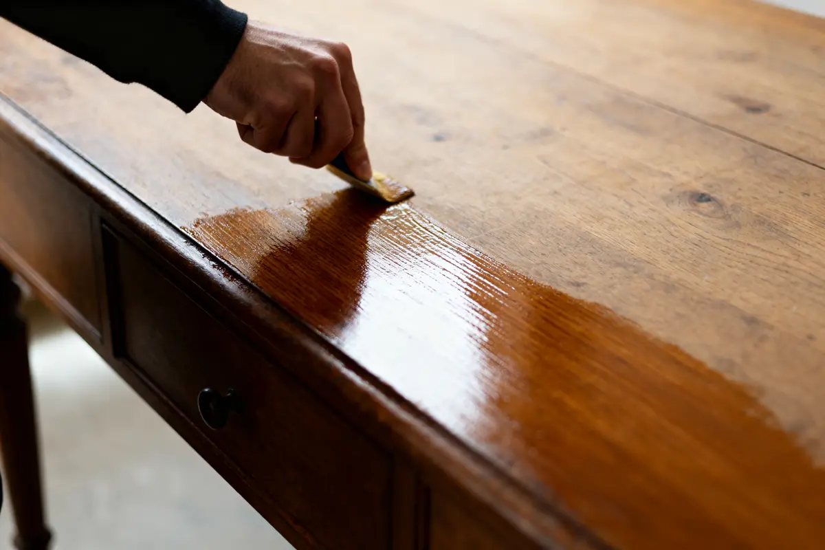 Main passant une brosse pour enlever du vernis sur du bois d'une table en bois
