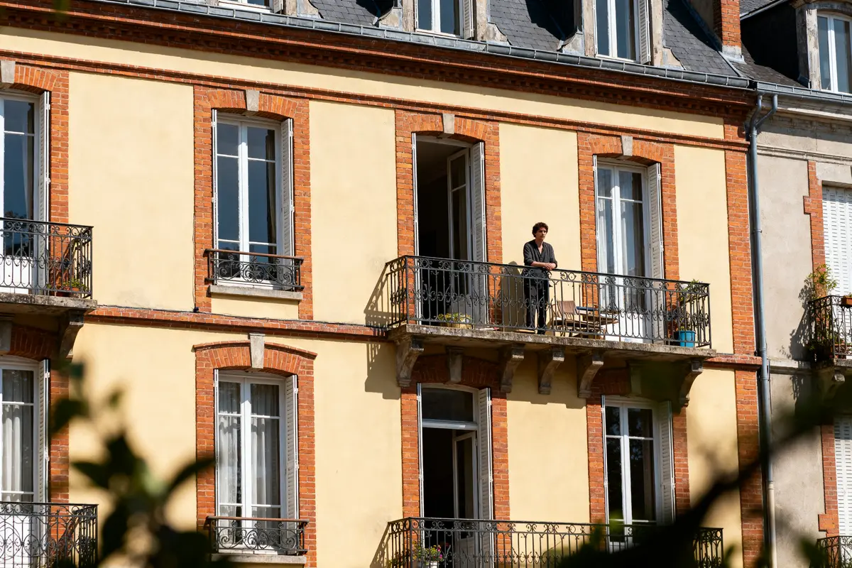 Façade de maison années 30 avec balcon et personne debout en extérieur