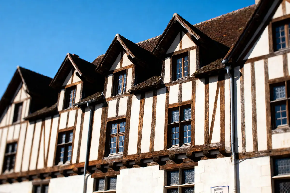 Façade de maison à colombages avec fenêtres en bois sous un ciel bleu clair.