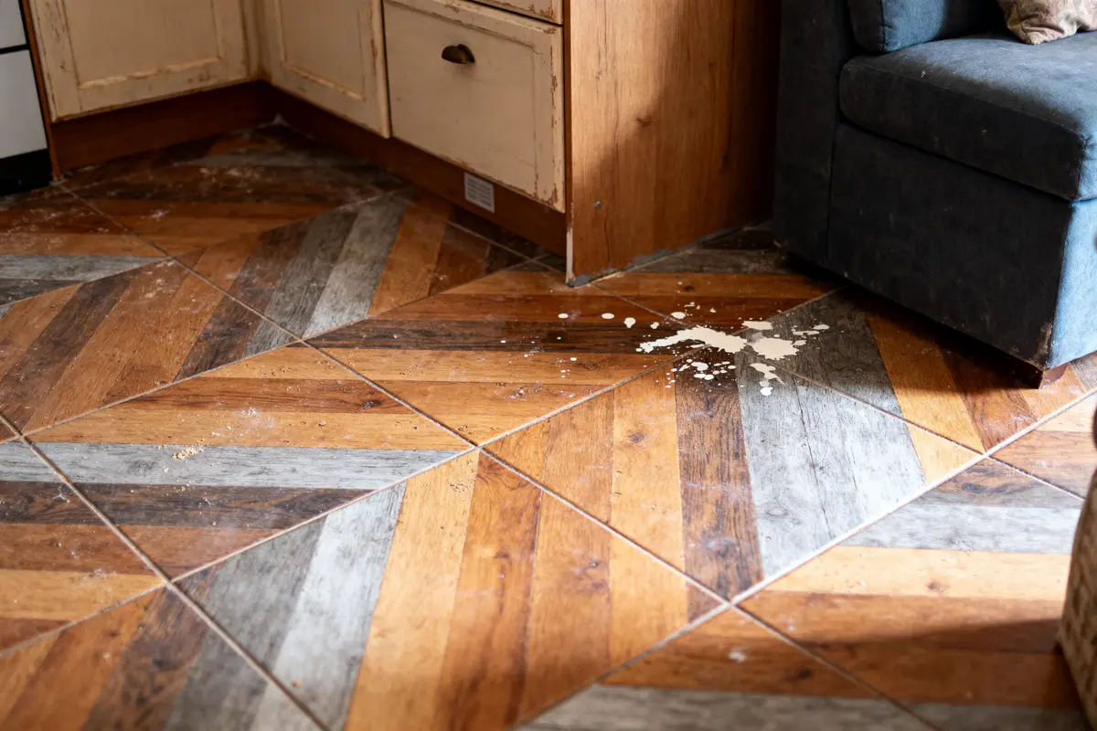 Carrelage en chevrons avec tache de liquide blanc près des meubles de cuisine et canapé bleu.