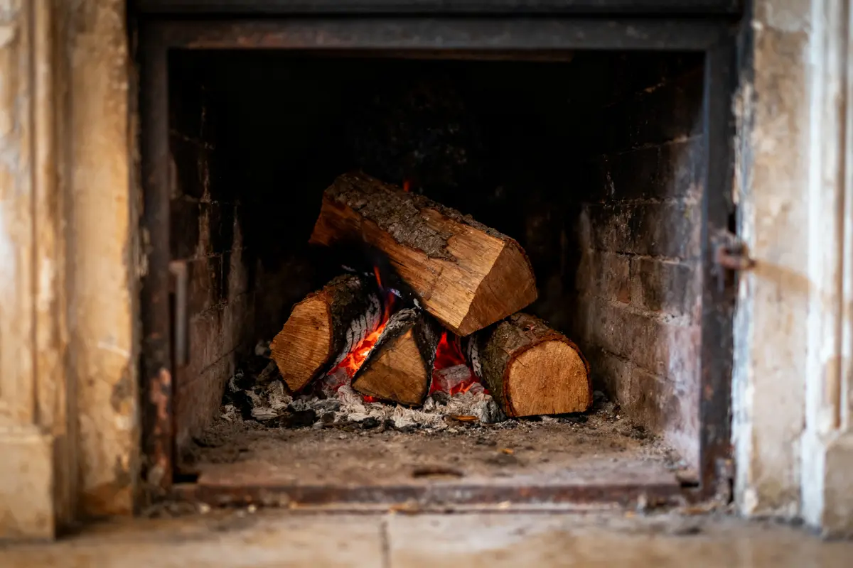 Bûches brûlant dans une cheminée en pierre avec des flammes rouges et des braises.